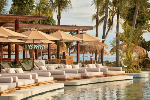 a resort pool with white lounge chairs and umbrellas at Paradisus by Meliá Bali in Nusa Dua
