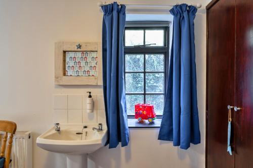 a bathroom with a sink and a window with blue curtains at Finest Retreats - Trimstone Manor, Manor Cottage in Woolacombe