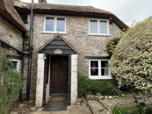 a stone house with a brown door and two windows at Ivy Cottage in West Lulworth