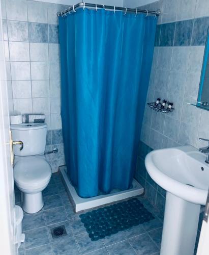 a bathroom with a toilet and a blue shower curtain at Hotel Ilios in Kriopigi