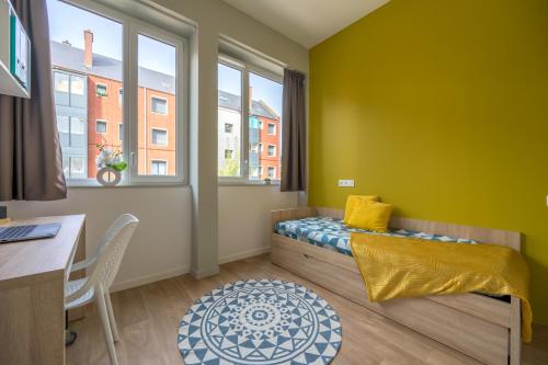 a small room with a bed and a desk and windows at Nemea Appart Hotel Coliseum Amiens Centre in Amiens