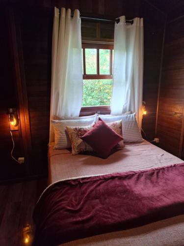 a bed with a window with white curtains and pillows at Chalé Ipê Amarelo in Juquitiba