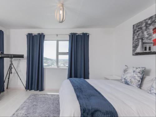 a bedroom with a bed with blue curtains and a window at Poolstreet 18 in Agulhas