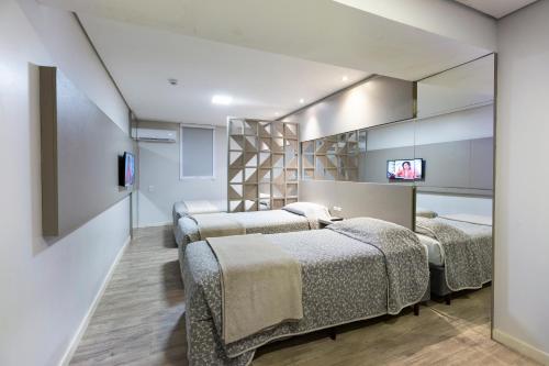 a room with four beds and a tv on a wall at Hotel Palmas Executivo in Balneário Camboriú
