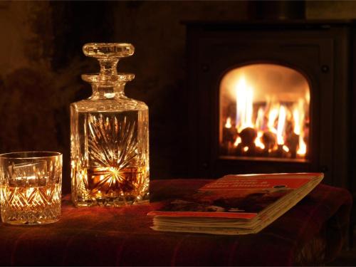 a table with a glass bottle and a book and a fireplace at 2 Bed in Birnam Dunkeld oc-ca266 in Birnam