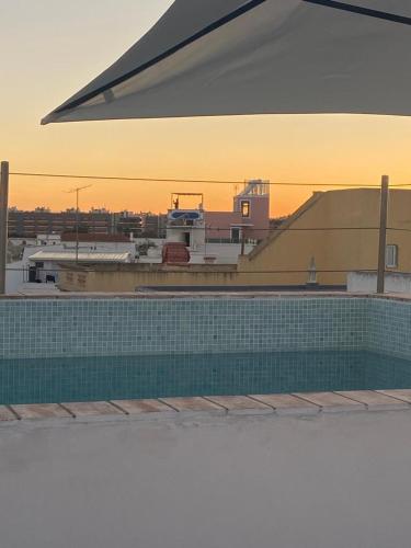 a swimming pool in front of a building with the sunset at Casa Opala Townhouse met Rooftop Pool in Olhão