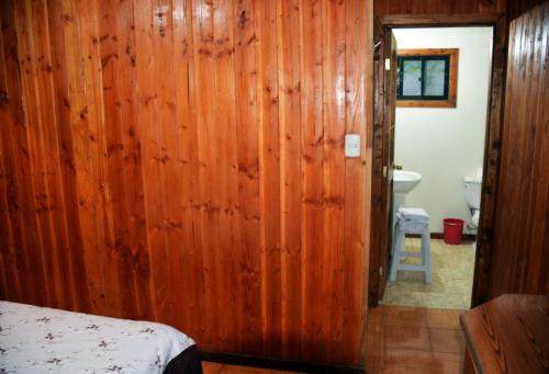 a bedroom with a wooden wall and a bathroom at Refugio Ruka Cümelen in Panguipulli