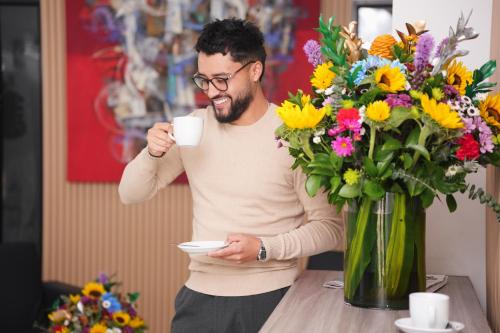 a man holding a cup of coffee next to a vase of flowers at Hotel Regency Boutique La Feria in Bogotá