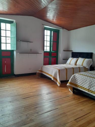 two beds in a room with wooden floors and windows at Posada La Casona in El Cocuy