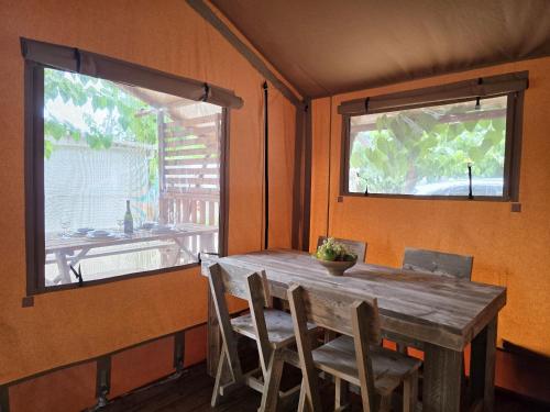 a dining room with a wooden table and two windows at Camping Costa Dorada Tienda Lua in Canet de Mar