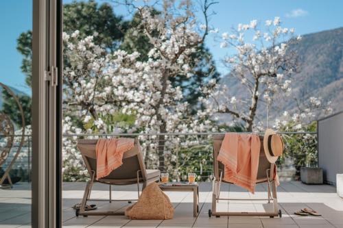 two chairs and a table on a balcony with flowering trees at Villa Hochland in Merano