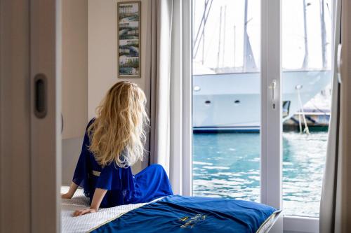 a woman sitting on a bed looking out a window at Floating House Royal Blue Portorož in Portorož