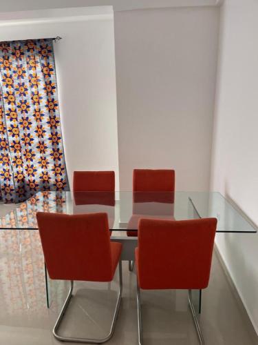 a glass table with four red chairs in a room at sempri djuntu T1A in Tarrafal