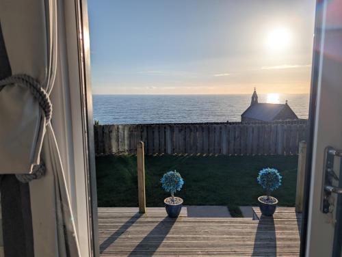 an open door with two potted plants looking out at the ocean at Allibella Shepherds Hut, Amazing Seaview, Private garden, Pet Friendly in Barmouth