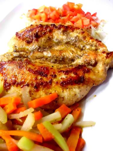 a piece of chicken with vegetables on a white plate at Hotel Cabanas La Teca in Liberia
