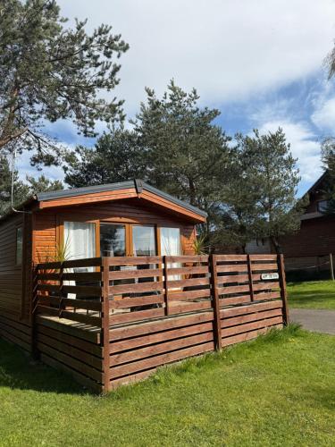 a wooden cabin with a fence in the grass at Happy Ever After Lodge in Morpeth