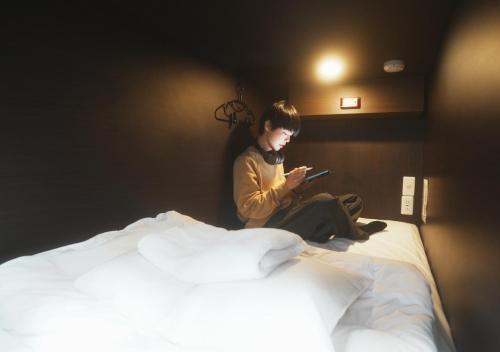 a man sitting on a bed looking at his cell phone at Hostel JAZ in Tokyo