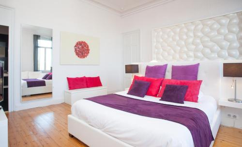 a white bedroom with a large bed with red and purple pillows at L'Esplanade Lille in Lille