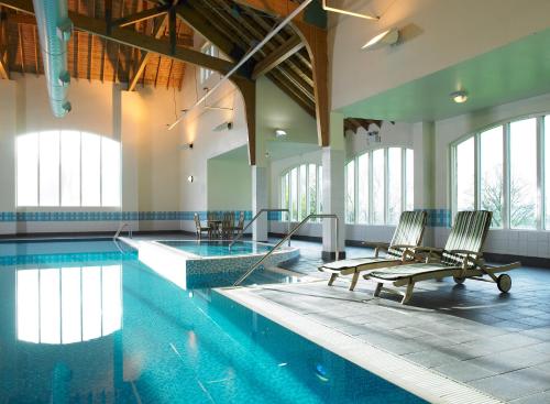 a swimming pool with two chairs in a building at Hollins Hall Hotel, Golf & Country Club in Bradford
