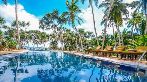 una piscina con sillas y palmeras en Sanjis The Seaside Cabanas, en Tangalle