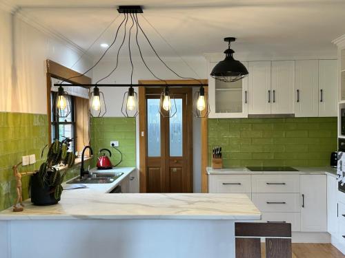 a kitchen with white cabinets and green tiles at Tarkine Retreat in Penguin