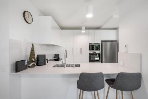 a white kitchen with two chairs and a clock at Pawfect Coastal - Pet friendly Beachfront Pool in Marcoola