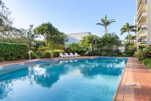 a swimming pool with chairs and a building at Coastal Drift - Beach Access Pool Spa Gym in Marcoola
