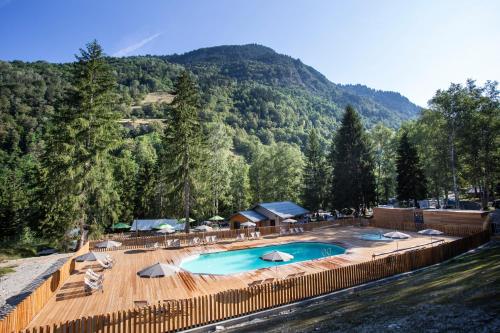 a swimming pool with chairs and umbrellas next to a mountain at Huttopia Bozel en Vanoise in Bozel