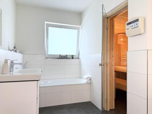 a white bathroom with a sink and a bath tub at Diemelblick 22 - SEEBLICK in Heringhausen