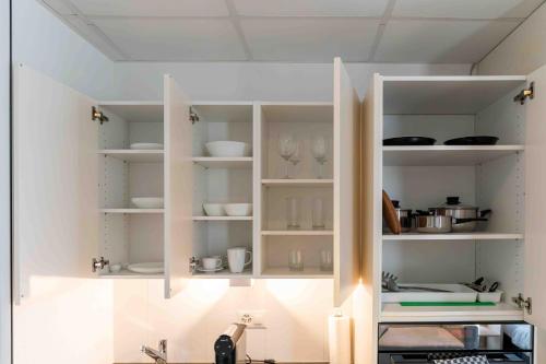 a kitchen with white shelves with dishes and glasses at Los Lorentes Hotel Bern Airport in Belp