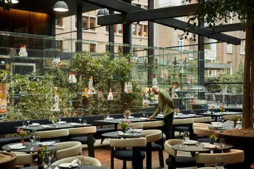 a man standing in a restaurant with tables and chairs at Mandarin Oriental Conservatorium, Amsterdam in Amsterdam