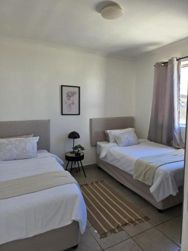 a bedroom with two beds and a table and a window at The041Stay in Gqeberha