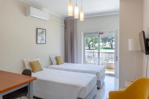 a hotel room with two beds and a desk and a window at Kiss - Apartamentos in Albufeira