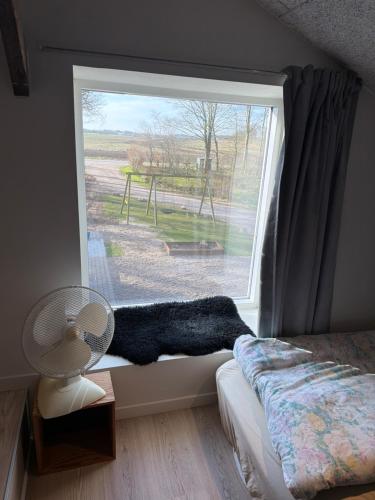 a bedroom with a window with a bed and a fan at Højmosegård ÅBENT HEMS in Varde