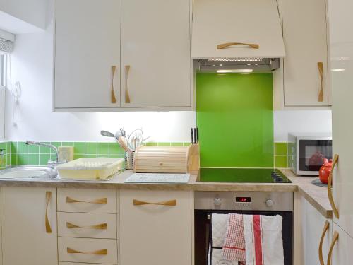 a kitchen with white cabinets and a green wall at Stockdale Cottage in Ambleside