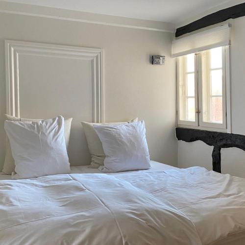 a white bed with white pillows and a window at Købmandsgården, Ballen in Ballen