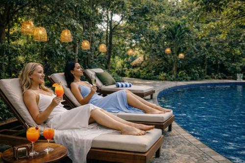 two women sitting in chairs next to a swimming pool at Sundaras Infinity Jungle Resort & Spa in Dambulla