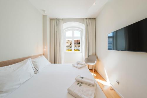 a white bedroom with a large bed and a television at Liberator Rossio in Lisbon
