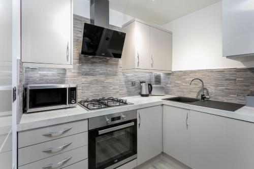 a white kitchen with white cabinets and a microwave at Forbes Retreat - Donnini Apartments in Ayr