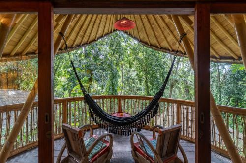 a hammock on a screened in porch with chairs at Bamboo Turtles Ecolodge in Ubud