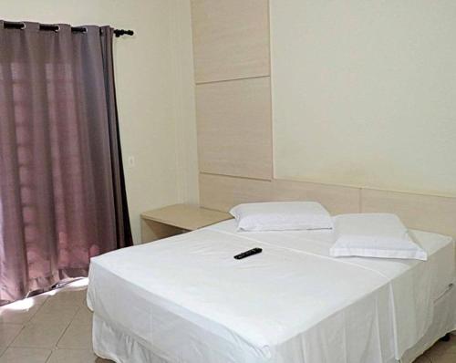 a bedroom with a white bed with a remote control on it at Pousada Gran-Café in Quixadá
