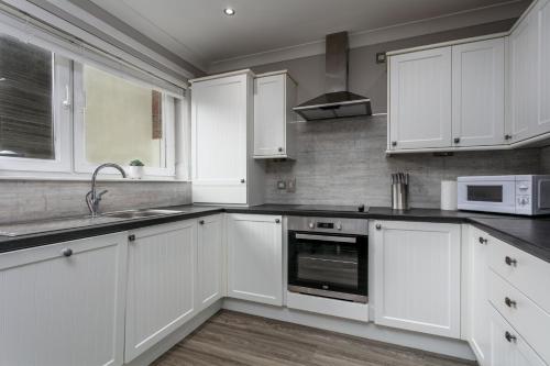 a kitchen with white cabinets and a sink and a microwave at Iona Residence - Donnini Apartments in Ayr