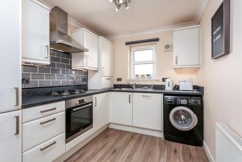 a kitchen with white cabinets and a washer and dryer at The Lucas - Donnini Apartments in Ayr