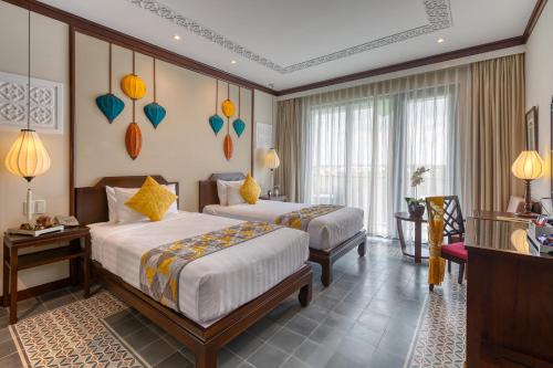 a hotel room with two beds and a table at Savvy in Hoi An - The Essence of Refined Retreat in Hoi An