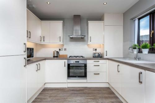 a white kitchen with white cabinets and a window at The Huntington - Donnini Apartments in Ayr