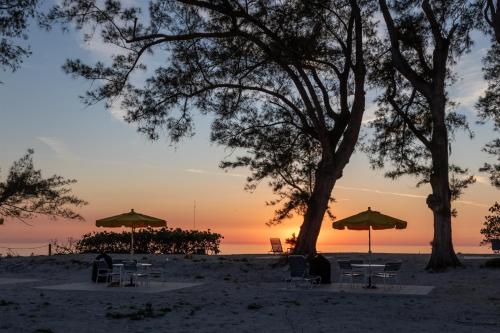 a sunset on the beach with tables and umbrellas at Bamboo Apartments in Holmes Beach
