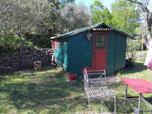 a green and red shed with a table and a chair at Cabane sous les oliviers in Saint-Ambroix