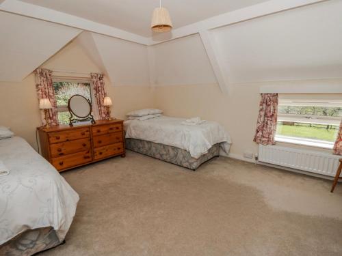 a bedroom with two beds and a dresser and two windows at Riverside Cottage in Llandrindod Wells