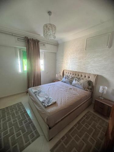 a bedroom with a large bed with a chandelier at Résidence Al kawtar, Mimosa Appartement in Ben Slimane
