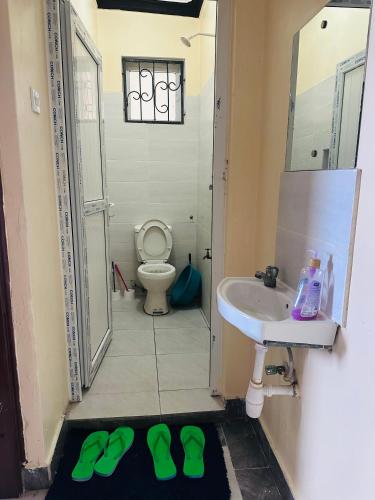 a bathroom with a sink and a toilet with green slippers at Honed homes in Mombasa
